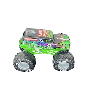 May include: A toy monster truck with large black tires and a green chassis. The truck's body is black with green and orange flame graphics and the words "Grave Digger" and a skull design.