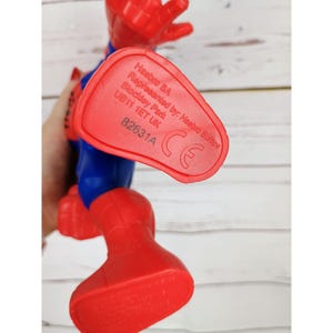 Puede incluir: Figura de acci&oacute;n de pl&aacute;stico rojo y azul de un superh&eacute;roe con un pie rojo que muestra el texto "Hasbro SA Represented by: Hasbro Europe Stockley Park UB11 1ET UK 82631A CE"