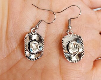 May include: A pair of silver dangle earrings with a cowboy hat charm. The hats have a silver rope design around the brim.