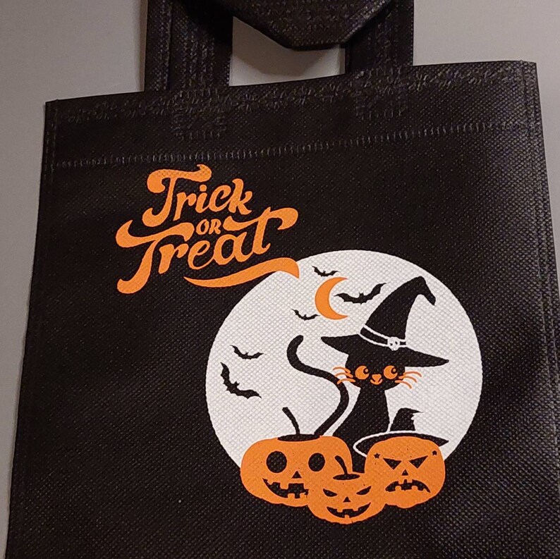 May include: Black reusable tote bag with a white moon and black cat wearing a witch hat. The bag has the text "Trick or Treat" in orange lettering.