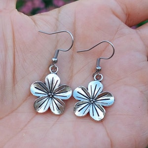 May include: A pair of silver flower-shaped earrings with a delicate design. The earrings have a simple hook closure.