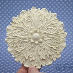 May include: A white, decorative ceiling medallion with a floral design. The medallion is made of plaster and has a raised, intricate pattern of leaves and flowers.