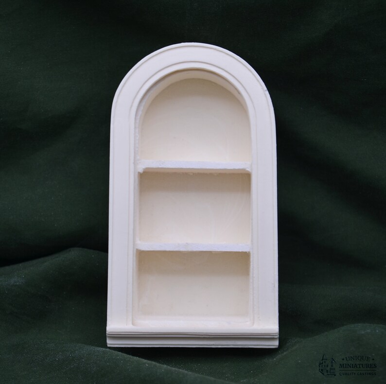 May include: White arched shelf unit with three shelves. The shelf unit is made of plaster and has a smooth finish.