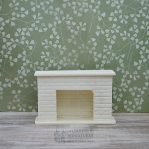 May include: White miniature brick fireplace with a mantel and a rectangular opening. The fireplace is on a light wood surface in front of a green background with a white floral pattern.