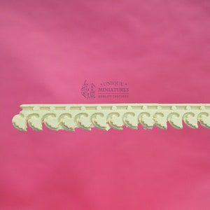 May include: White decorative trim with a repeating pattern of stylized leaves. The trim is made of a lightweight material and is designed for use in dollhouses or miniature projects. The trim is labeled "Unique Miniatures Quality Castings".