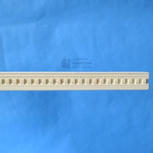 May include: A white, decorative molding with a repeating pattern of squares and circles. The molding is made of a lightweight material and is designed for use in dollhouses or miniature projects. The text "UNIQUE MINIATURES QUALITY CASTINGS" is printed on the molding.