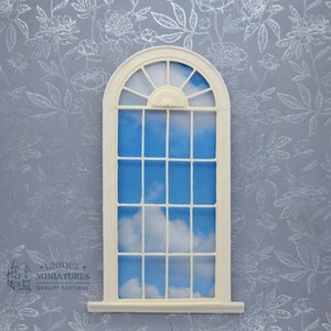 May include: A miniature arched window with a grid of small panes, painted in a cream color. The window frames a bright blue sky with fluffy white clouds. The background is a floral wallpaper in shades of gray. The text "UNIQUE MINIATURES QUALITY CASTINGS" is visible.