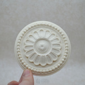 May include: White plaster ceiling medallion with a raised floral design and a beaded border.