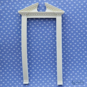 Könnte beinhalten: Weißer Miniatur-Türrahmen mit einem dekorativen Oberteil, vor einem blau-weiß gemusterten Hintergrund.