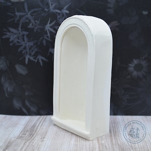Puede incluir: Estante de nicho blanco en forma de arco hecho de yeso o resina. El estante tiene una parte superior redondeada y una pequeña repisa. El estante está diseñado para casas de muñecas o escenarios en miniatura.