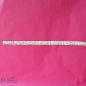 May include: A white decorative trim with a repeating pattern of leaves and beads. The trim is on a pink background.
