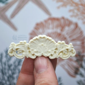 May include: White decorative trim with a shell design. The trim is made of a lightweight material and has a delicate, intricate design. It is perfect for adding a touch of elegance to any project.