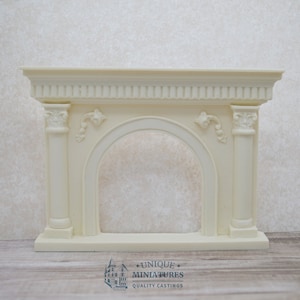 Op de afbeelding: Wit geschilderde miniatuur open haard met een decoratieve gebogen opening en gegroefde kolommen. De open haard is gemaakt van hars en is ontworpen voor poppenhuizen of miniatuur settings.