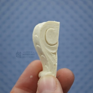 Puede incluir: Una pieza decorativa de resina blanca con un diseño detallado de un rollo y una luna creciente. La pieza se sostiene en una mano, mostrando su tamaño y detalle.