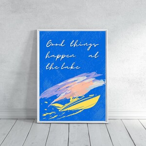 以下が含まれることがあります： 青い背景に「Good things happen at the lake」というテキストが入った額入りのアートプリント。画像には、上にカラフルな筆致のある黄色のスピードボートが描かれています。アートワークは白い壁に表示されています。