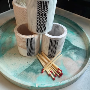 May include: A set of decorative match holders and a tray. The cylindrical holders are white with a black honeycomb pattern. Some holders contain red-tipped matches. The tray is teal and white.