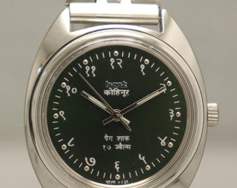 Puede incluir: Reloj de pulsera plateado con esfera verde oscuro y correa plateada a juego. La esfera del reloj presenta números arábigos y texto en idioma extranjero. El reloj se muestra sobre un fondo neutro.