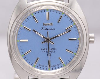 Puede incluir: Un reloj de pulsera Kohinoor vintage con esfera azul claro y caja plateada. El reloj presenta una correa de cuero negro y el texto "PARA SHOCK 17 JEWELS". El reloj está marcado "MADE IN INDIA 0231".