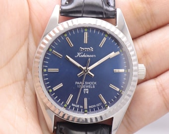 Puede incluir: Un reloj Kohinoor Parashock plateado con esfera azul oscuro y correa de cuero negro. La esfera del reloj presenta agujas e indicadores plateados, con el texto "PARASHOCK 17 JEWELS" y "MADE IN INDIA 0231".
