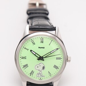 May include: Silver-tone wristwatch with a light green face featuring Snoopy and Roman numerals. The watch has black hands and a black leather band. The word "hmt" is printed on the watch face.