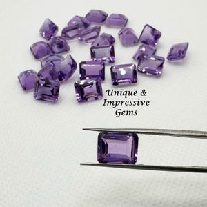May include: A collection of faceted, rectangular amethyst gemstones in various sizes. One gem is held by tweezers, showcasing its deep purple color. The image includes the text "Unique & Impressive Gems".