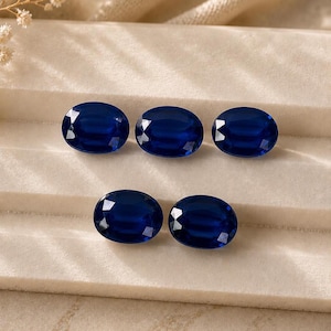 May include: Five oval-cut, deep blue gemstones arranged in two rows. The top row contains three stones, and the bottom row contains two stones. Each gemstone features a faceted surface that reflects light, creating a brilliant, polished appearance.