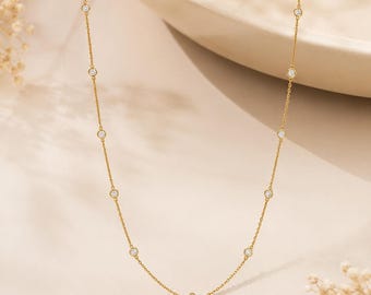 Könnte beinhalten: Eine zarte Goldkettenhalskette mit gleichmäßig verteilten, runden, in Zargenfassung gefassten klaren Steinen. Die Halskette besteht aus einer feingliedrigen Kette, die mehrere kleine, kreisförmige, funkelnde Steine in einem gleichmäßigen Muster hält.