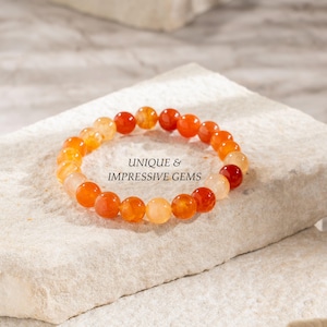 Puede incluir: Un brazalete hecho de cuentas de piedras preciosas de color naranja y amarillo. El brazalete está sobre una superficie blanca. UNIQUE & IMPRESSIVE GEMS