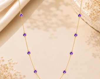 Könnte beinhalten: Eine goldene Halskette mit gleichmäßig verteilten, runden, leuchtend violetten Edelsteinen in Goldfassungen. Die feinen Kettenglieder verbinden jeden Stein zu einem durchgehenden Collier-Design, das in einer sanften, symmetrischen Kurve hängt.