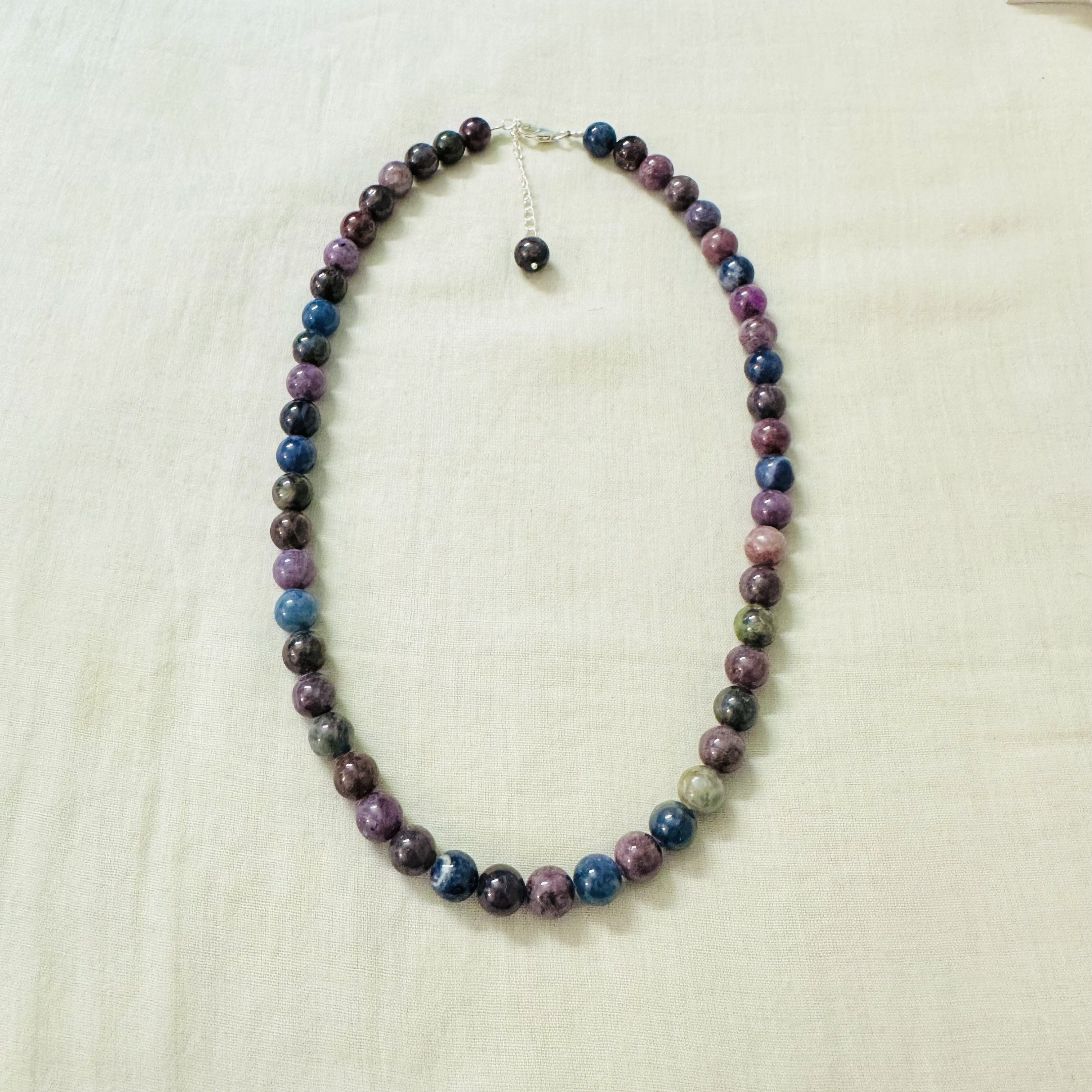 K&ouml;nnte beinhalten: Halskette mit runden Perlen in verschiedenen Farben, darunter Lila, Blau und Gr&uuml;n. Die Kette hat einen silberfarbenen Verschluss. Die Perlen haben einen Durchmesser von etwa 1,3 cm.