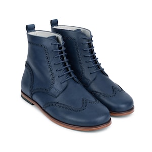 May include: A pair of navy blue leather ankle boots featuring a classic wingtip brogue design with decorative perforations along the seams, matching blue laces, a pull tab at the heel, and a low-profile brown sole with a stacked heel finish.