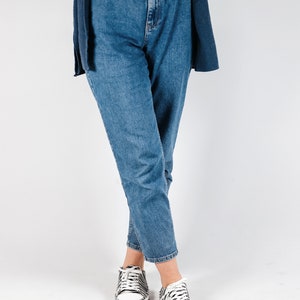 May include: A person wearing blue jeans with a black belt and white sneakers with black and white zebra print.
