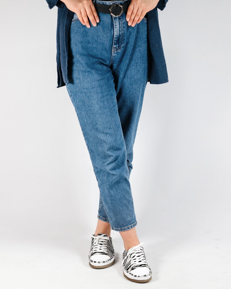 May include: A person wearing blue jeans with a black belt and white sneakers with black and white zebra print.