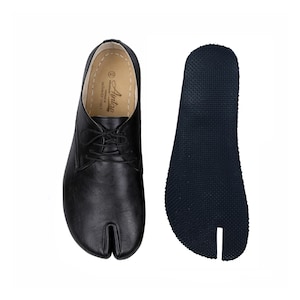 May include: Black leather split-toe shoes with laces, and a separate dark blue rubber sole. The shoes have a unique design with a split between the big toe and the other toes. The sole is textured for grip. The shoes are likely for casual wear.