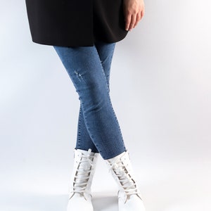 Pu&ograve; includere: Una persona che indossa un blazer nero, jeans blu e stivali bianchi con lacci.
