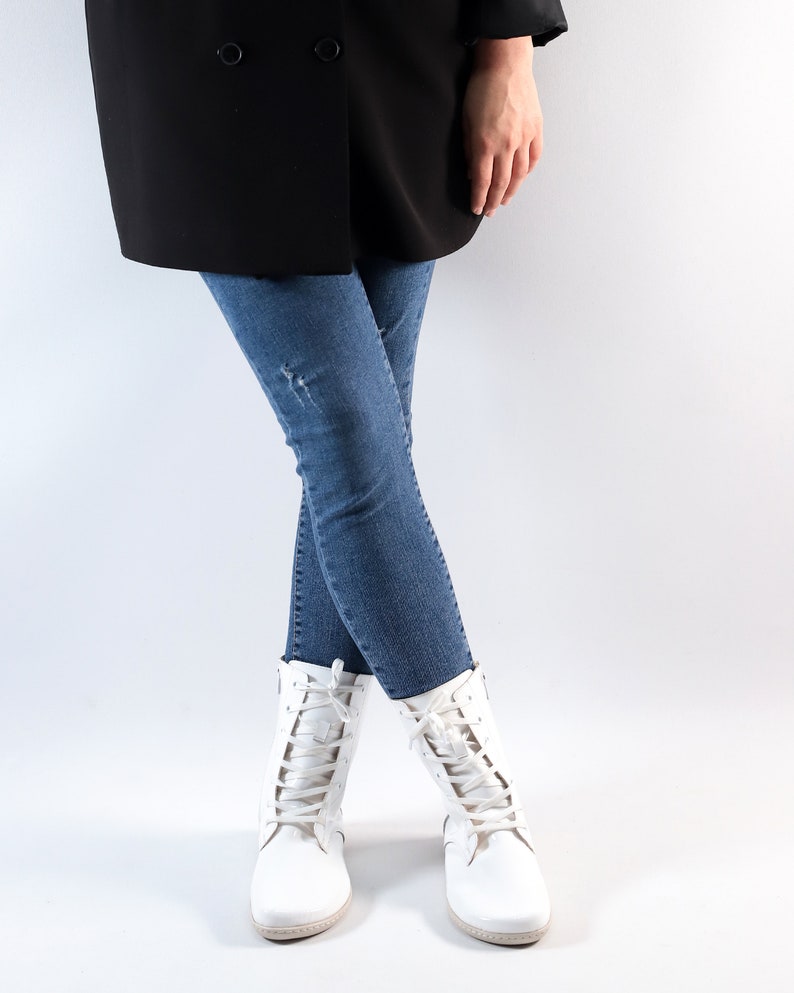 Pu&ograve; includere: Una persona che indossa un blazer nero, jeans blu e stivali bianchi con lacci.
