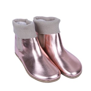 Puede incluir: Botines color oro rosa con acabado metálico. Cuentan con un puño de punto gris claro doblado y una suela marrón claro. Las botas tienen un panel elástico en el lateral. Calzado elegante.