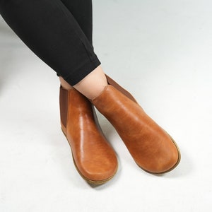 May include: A pair of brown leather ankle boots with elastic side panels. The boots have a rounded toe and a low heel.