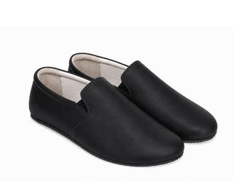 May include: A pair of black slip-on shoes featuring a smooth matte exterior, a rounded toe, and a light-colored interior lining. The shoes have a low-profile design with black elastic side gussets and a thin, textured black rubber sole.