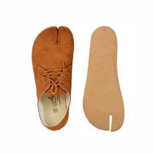 May include: A pair of brown split-toe shoes with laces, alongside a matching insole. The shoes have a suede-like texture and a unique design separating the big toe. The insole is a light brown color with a textured surface.