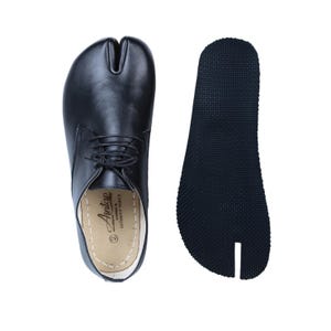 Op de afbeelding: Zwarte leren schoen met splitteen en veters, naast een zwarte rubberen zool. De schoen heeft een uniek ontwerp met een aparte ruimte voor de grote teen. De zool is getextureerd voor grip. Schoenmaat 42.
