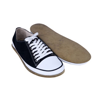 May include: A pair of black and white canvas sneakers with white laces. The sneakers have a brown rubber sole and are lying on a white background.