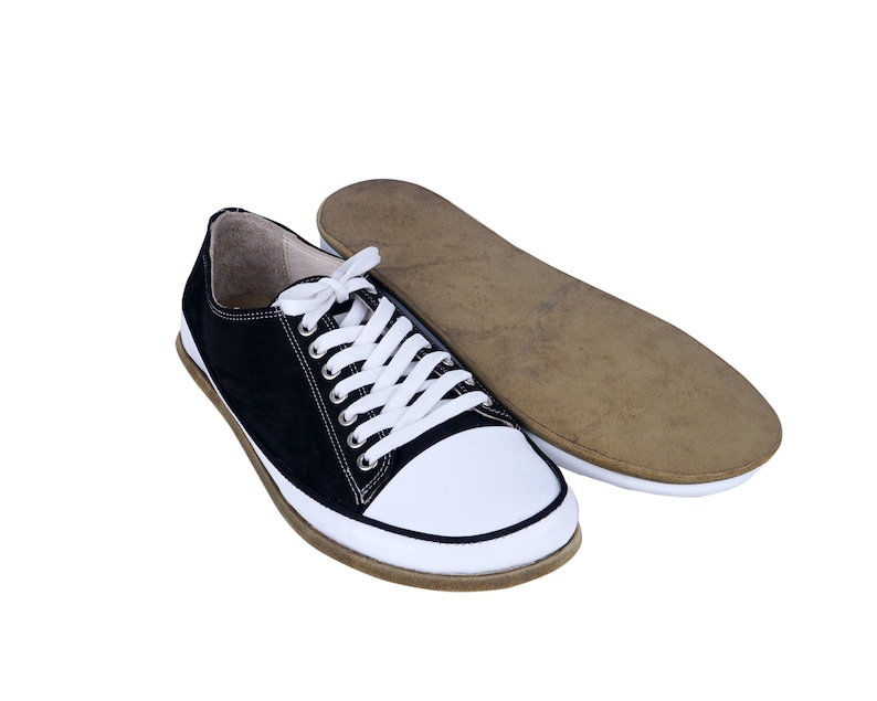 May include: A pair of black and white canvas sneakers with white laces. The sneakers have a brown rubber sole and are lying on a white background.