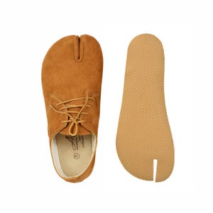 Puede incluir: Zapatos Tabi de ante marrón claro con diseño de puntera dividida, cierre de cordones y plantilla separada. Los zapatos son de color marrón claro. Talla 38.