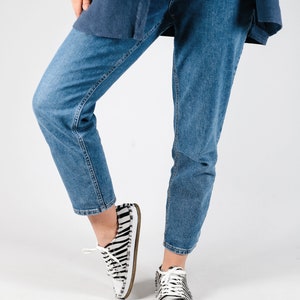 May include: A person wearing blue jeans and white and black zebra print sneakers.