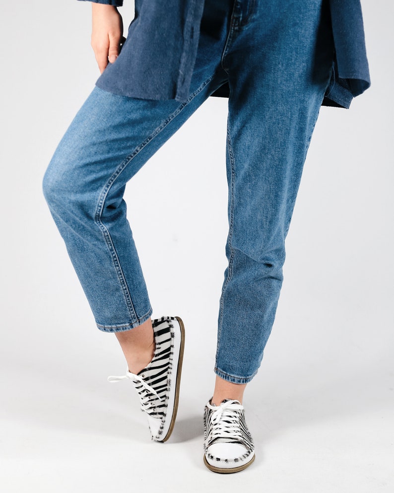 May include: A person wearing blue jeans and white and black zebra print sneakers.