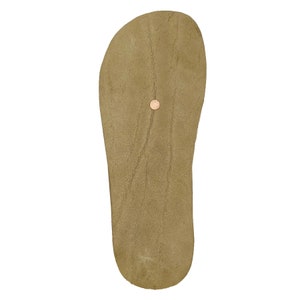 May include: A tan-colored leather sandal sole with a smooth, matte texture and a rounded toe shape. A single small, circular copper-toned metal rivet is embedded in the center of the footbed, providing a distinct point of contrast on the surface.