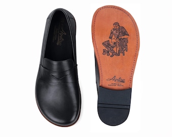 May include: Black leather loafers with a classic design, one showing the sole with a craftsman illustration and the brand name. The other shoe displays the top view. The soles are dark, and the interior is tan.