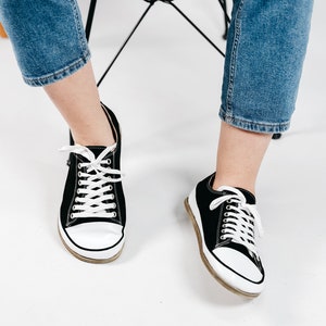 May include: A pair of black canvas low top sneakers with white laces and white soles.