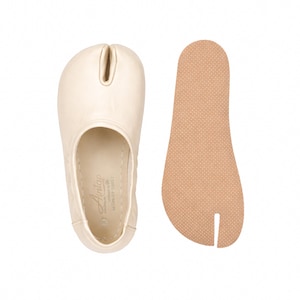 May include: Cream-colored split-toe shoe with a separate beige insole. The shoe has a rounded toe and a split for the big toe. The insole is textured. The shoe is likely made of leather.